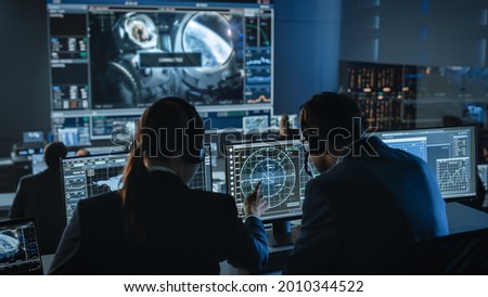 Group of People in Mission Control Center Establish Successful Video Connection on a Big Screen with an Astronaut on Board of a Space Station. Flight Control Scientists Sit in Front Computer Displays.