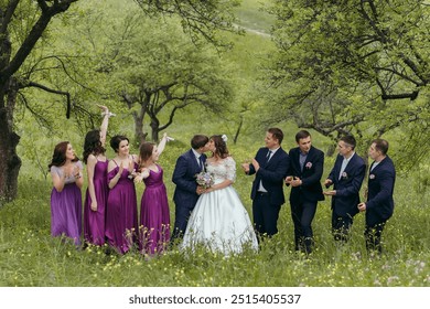 A group of people are posing for a picture in a field. The bride and groom are in the center of the group, with the other people surrounding them. The bride is wearing a white dress - Powered by Shutterstock