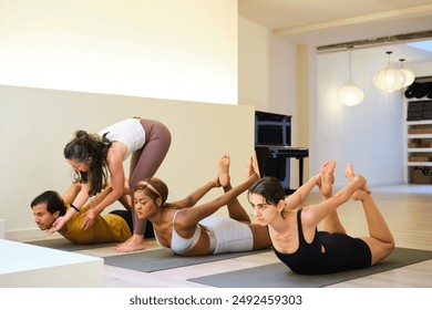 A group of people practicing dhanurasana or the bow yoga pose and the instructor helping. Yoga class. - Powered by Shutterstock