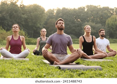 Group of people practicing yoga on mats outdoors. Lotus pose - Powered by Shutterstock