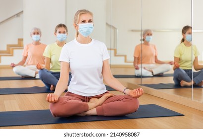 Group Of People In Protective Mask Sitting In Lotus Position Practicing Meditation In Yoga Class