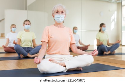 Group Of People In Protective Mask Sitting In Lotus Position Practicing Meditation In Yoga Class