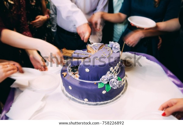 a group of people share a large purple\
wedding cake. Sweets at the party.\
Wedding
