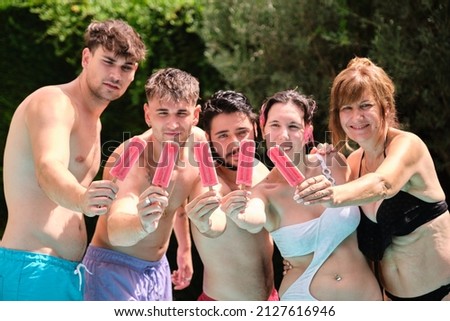 Group of people showing strawberry popsicles to the camera and having fun at the swimming pool.