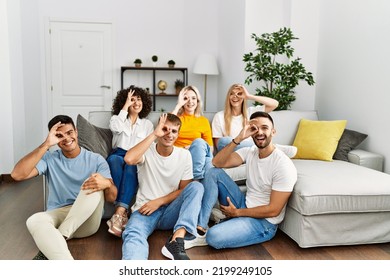 Group Of People Sitting On The Sofa And Floor At Home Smiling Happy Doing Ok Sign With Hand On Eye Looking Through Fingers 