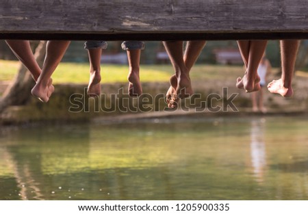 group of  people sitting at wooden bridge over the river with a focus on hanging legs