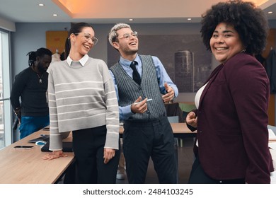 A group of people are smiling and laughing together in a room. The man is wearing a tie and the woman is wearing a striped sweater - Powered by Shutterstock