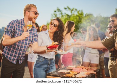 Group of people standing around grill, chatting, drinking and eating.  - Shutterstock ID 1117436672