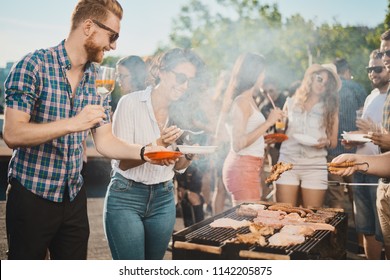 Group of people standing around grill, chatting, drinking and eating.  - Shutterstock ID 1142205875