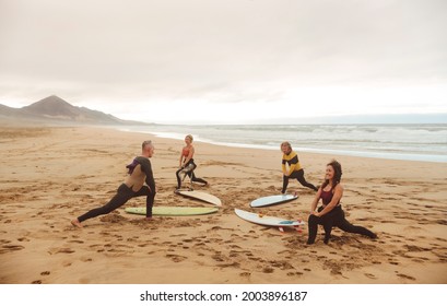 Group of people stretching at the beach, before starting a surf session. - Sportive people warming up before going in the water. - Powered by Shutterstock