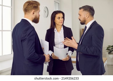 Group Of People In Suits Having A Conversation. Three Serious Business Professionals Discussing Something. Defendant, Defense Lawyer And Relative Standing In Courtroom, Holding Documents And Talking