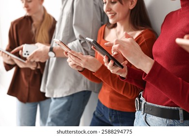Group of people using different gadgets near light wall indoors, closeup. Modern technology