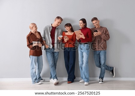 Group of people using different gadgets near light grey wall indoors. Modern technology