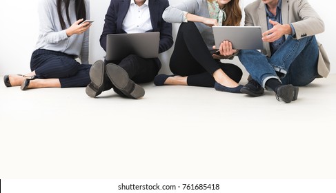 Group Of People Using Mobile Devices Sitting On The Floor.