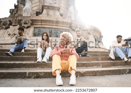 Group of people using phone with serious face. Friends focused on their mobiles siting on a bench outdoors in a park. Technology addicts concept. High quality photo