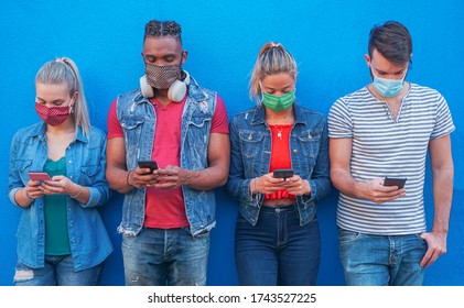 Group of people using their smartphones in covid 19 times protected with face mask - Friends checking online news while standing by the wall and holding cellphones