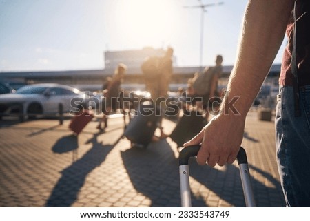 Group of people walking to airport terminal at summer sunset. Selective focus on hand of man with suitcase. 
