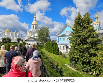 Group of people are walking down a path in front of a large building. The sky is cloudy and the atmosphere is calm and peaceful