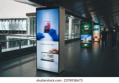 Group of people walking in public bridged walkway in station with blurred colorful digital signage advertisement board on passage in modern city at daylight
