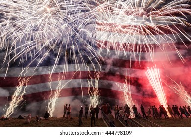 Group Of People Watching Colorful Fireworks In The Sky With American Flag In Background. 4th Of July Concept.