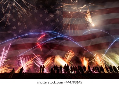 Group Of People Watching Colorful Fireworks In The Sky With American Flag In Background. 4th Of July Concept.