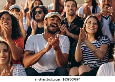 Group of people watching a sport event and cheering. Excited crowd of sports fans applauding sitting in stadium.