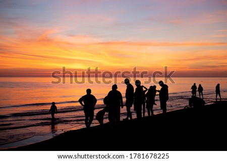 A group of people watching the sunset at the beach and forming a silouette