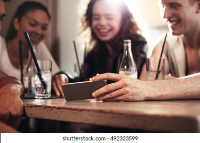 Group Of People Watching Video On The Mobile Phone While Sitting At Cafe. Young Friends Looking At Smartphone.