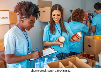 Group of people working in charitable foundation. Happy volunteer looking at donation box on a sunny day. Happy volunteer separating donations stuffs. Volunteers sort donations during food drive - Shutterstock ID 1692488662