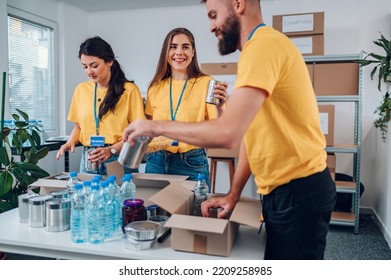 Group Of People Working On Humanitarian Aid Project. Teamwork In Homeless Shelter. Volunteers Working In A Community Charity Donation Center And Packing Food Into Cardboard Boxes. Copy Space. .