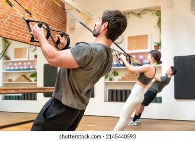 Group of people working out in a gym doing Trx low row exercises using suspension straps or bands to tone and strengthen their muscles