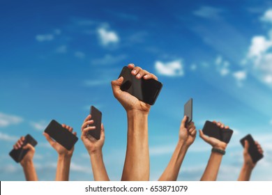 Group Of People's Hands Holding Phones And Rising Them Up Against Sky