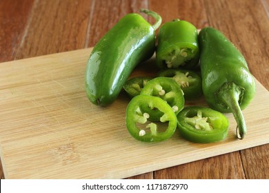 A Group Of Jalapeño Peppers With One Sliced On A Natural Wood Cutting Board