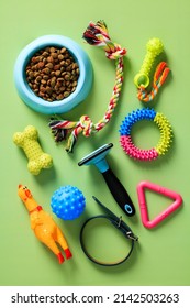 Group Of Pet Accessories, Bowl Of Dry Feed, Toys, Grooming Equipment On Green Table. Flat Lay, Top View, Overhead.