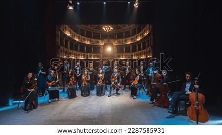 Group Photo: Portrait of Symphony Orchestra Performers on the Stage of a Classic Theatre, Looking at the Camera Together and Smiling. Successful and Professional Musicians Posing