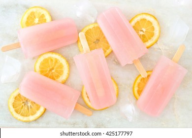 Group Of Pink Lemonade Popsicles With Lemon Slices, Ice Cubes On A White Marble Background