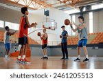 Group of players practicing with a ball during basketball training in school gymnasium.