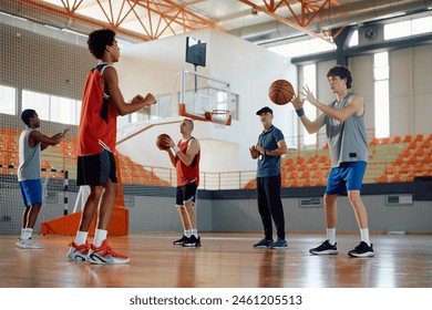Group of players practicing with a ball during basketball training in school gymnasium.