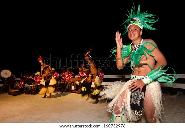 Group of Polynesian Pacific Island Tahitian\
male dancers dancing in colorful costume on tropical beach in\
Aitutaki Cook Islands..