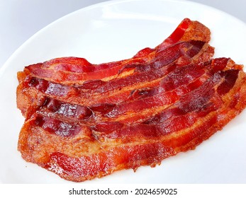 a group of pork bacon on white plate, close up and isolated in white background.