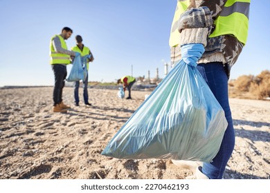 Group portrait of activists holding plastic waste. Teamwork standing up. Volunteers cleaning up rubbish in nature. Concept of environmental care. Blue garbage bag in foreground. - Powered by Shutterstock