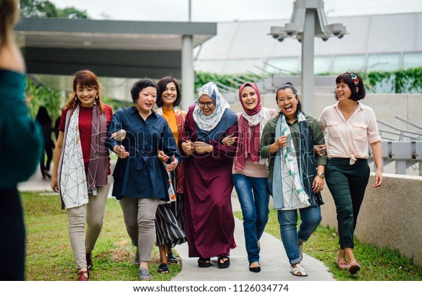 Group portrait of diverse group of women (Malay, Chinese\
and Eurasian) walking down a path in a housing estate in Singapore,\
Asia. They are friends and smiling as they walk and talk together.\
