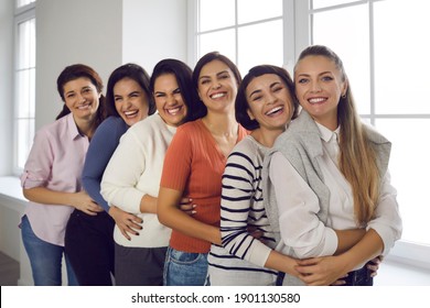 Group portrait of female friends hugging, smiling and looking at camera. Team of happy young women in their 20s and 30s standing in bright office and embracing each other. Concept of unity and support - Powered by Shutterstock