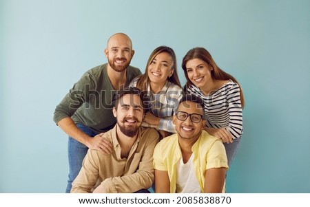 Group portrait of five happy, smiling mixed race multi ethnic friends. Team of 5 cheerful young diverse people with toothy smiles having photoshoot and looking at camera against blue studio background