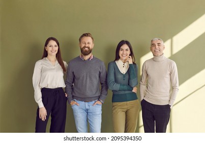 Group Portrait Of Four Happy People In Smart Casual Outfits Posing Against Green Studio Background. Team Of 4 Confident Business Men And Women Standing By Office Wall, Smiling And Looking At Camera