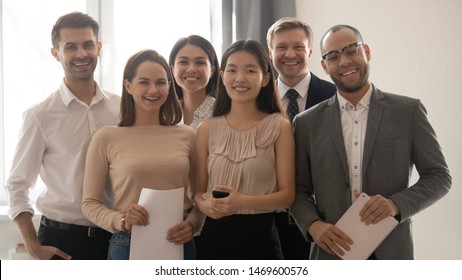 Group Portrait Of Happy Diverse Young Colleagues Stand Posing For Picture In Office Together, Multiethnic Smiling Millennial Coworkers Make Photo Show Team Unity And Support. Collaboration Concept