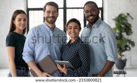 Group portrait of happy multiethnic united millennial team in modern office. Successful employees standing together, meeting in workspace, looking at camera and smiling Team work concept. Head shot