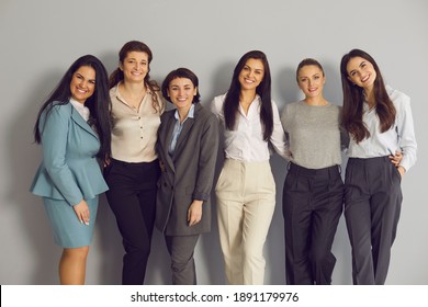 Group Portrait Of Happy Positive Business Women. Professional Team Of Successful Female Company Employees In Their 20s And 30s Standing Together Against Grey Studio Background And Smiling At Camera