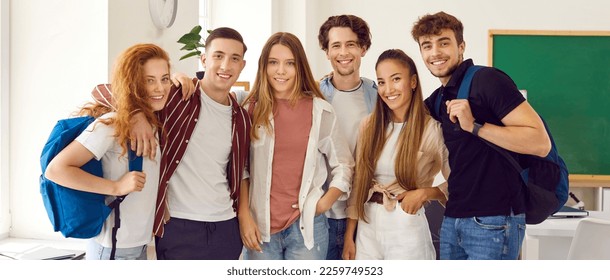 Group portrait of happy school, college or university friends. Several diverse young people with student backpacks standing together in the classroom, hugging, looking at camera and smiling - Powered by Shutterstock