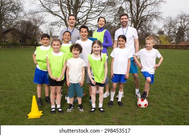 A Group Portrait Of A Kids Soccer Team, Behind Them Are Their Coaches. They Are All Smiling And Look Happy.